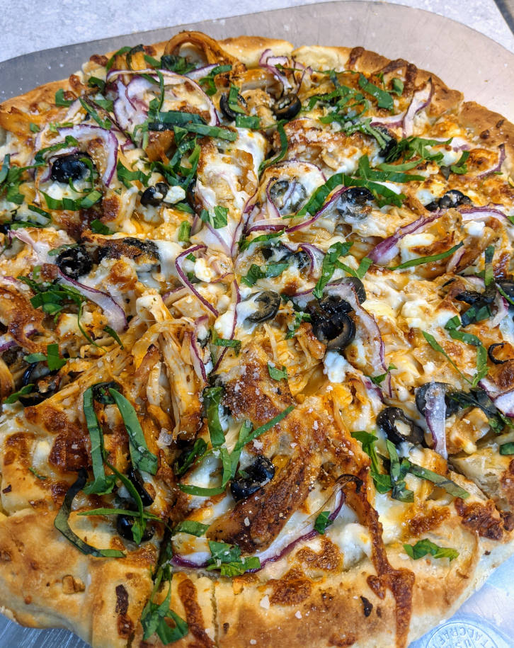 Close-up of a homemade chicken, olive and red onion pizza with fresh basil on top.